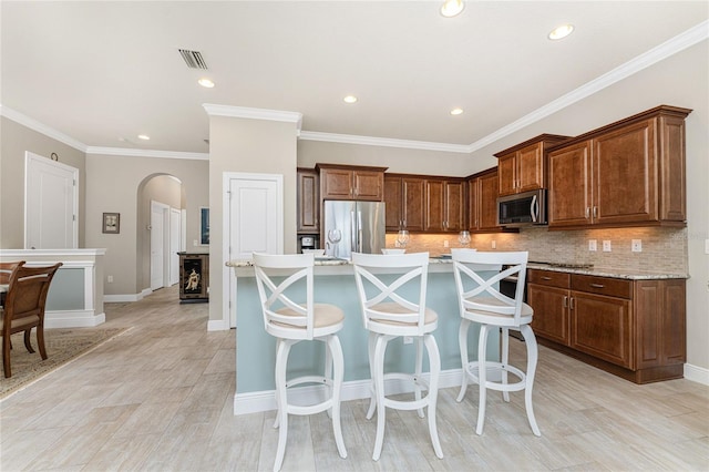 kitchen featuring a kitchen breakfast bar, decorative backsplash, an island with sink, and stainless steel appliances