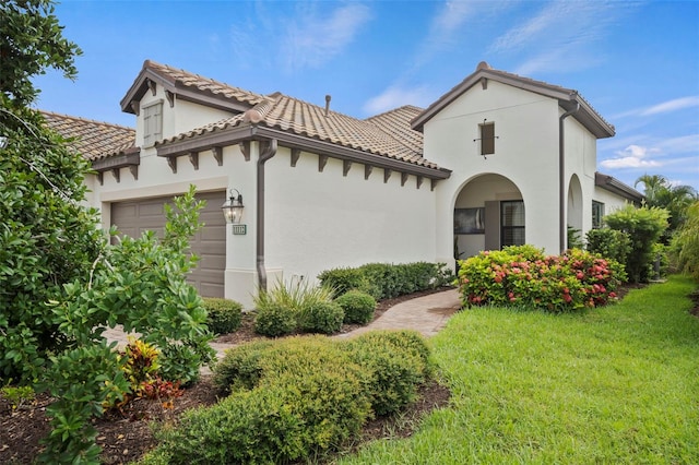 mediterranean / spanish house with a garage, a front yard, stucco siding, and a tiled roof