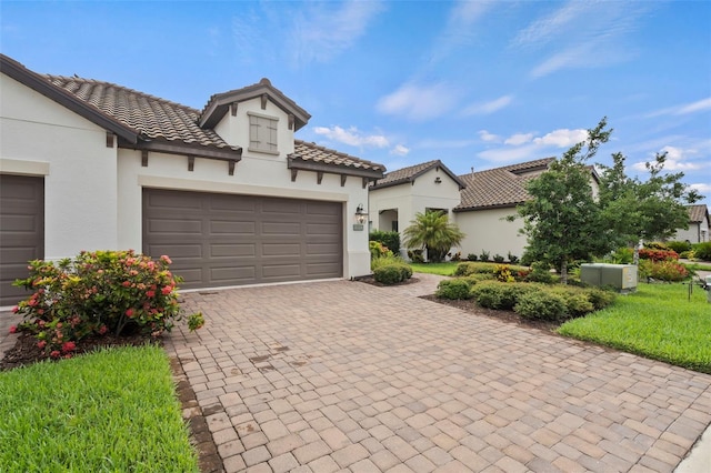 mediterranean / spanish-style house featuring stucco siding, an attached garage, a tile roof, and decorative driveway