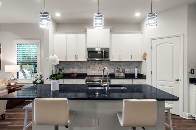 kitchen featuring a center island with sink, a kitchen breakfast bar, sink, decorative light fixtures, and white cabinetry