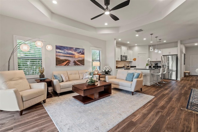 living room with a tray ceiling, ceiling fan, and dark hardwood / wood-style flooring