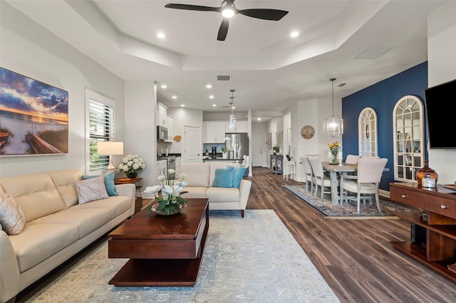 living area with visible vents, dark wood-type flooring, ceiling fan, a tray ceiling, and recessed lighting