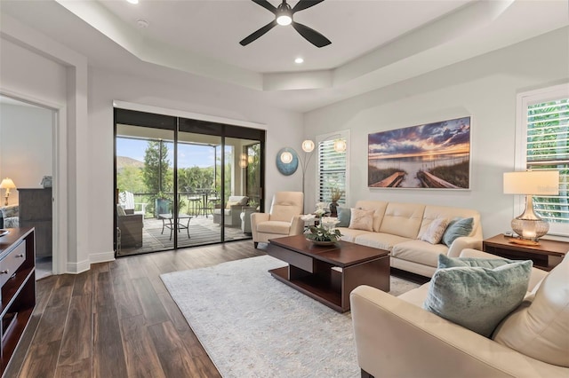 living room featuring ceiling fan, a raised ceiling, and dark wood-type flooring