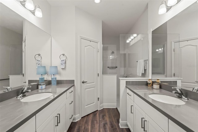 full bath with two vanities, wood finished floors, a tile shower, and a sink