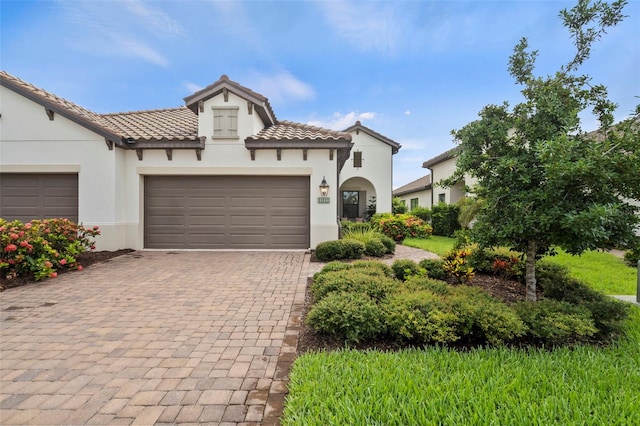 mediterranean / spanish house with decorative driveway, a tile roof, an attached garage, and stucco siding