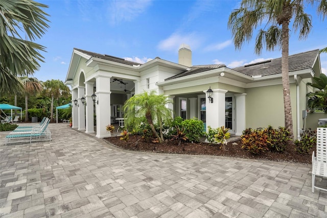 exterior space featuring a patio, stucco siding, a tile roof, and a chimney