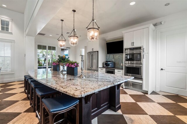 kitchen with backsplash, stainless steel appliances, decorative light fixtures, white cabinets, and a large island