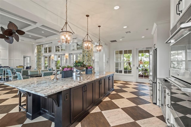 kitchen with a breakfast bar, stainless steel fridge, a spacious island, pendant lighting, and dark brown cabinets