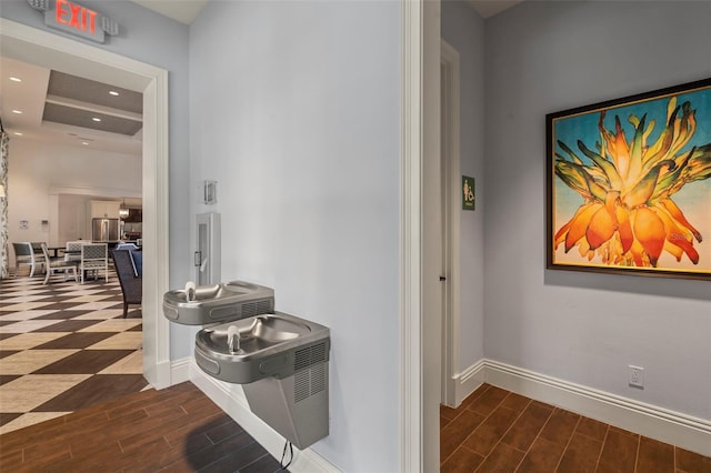 corridor featuring recessed lighting, baseboards, a tray ceiling, and wood finish floors