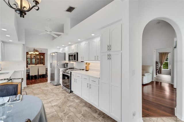 kitchen with a high ceiling, white cabinets, stainless steel appliances, and ceiling fan with notable chandelier