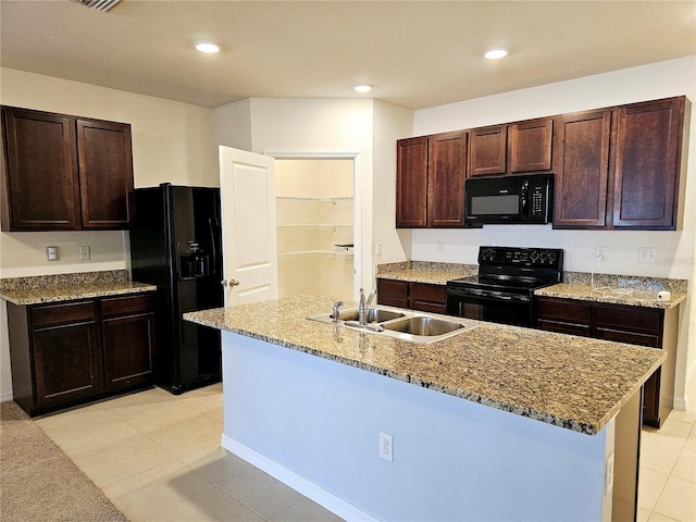 kitchen with black appliances, sink, light tile patterned floors, an island with sink, and light stone counters