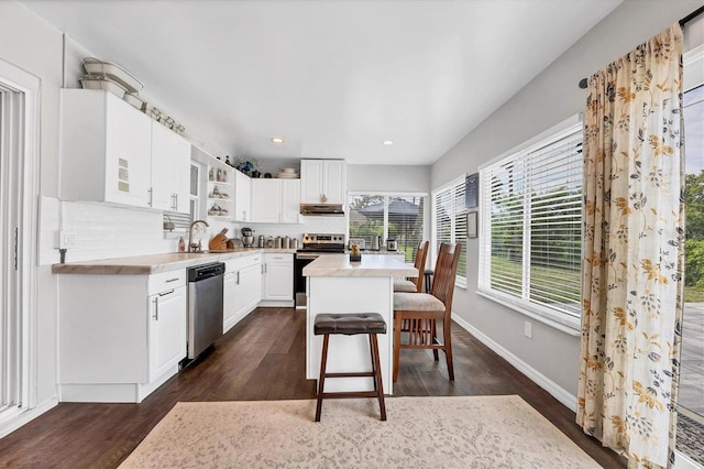 kitchen featuring dark hardwood / wood-style floors, tasteful backsplash, stainless steel appliances, white cabinets, and a kitchen bar