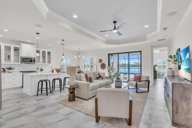 living room with a raised ceiling, ceiling fan with notable chandelier, and ornamental molding