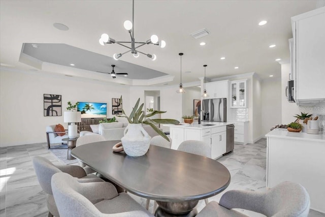 dining space featuring ceiling fan with notable chandelier, a tray ceiling, ornamental molding, and sink