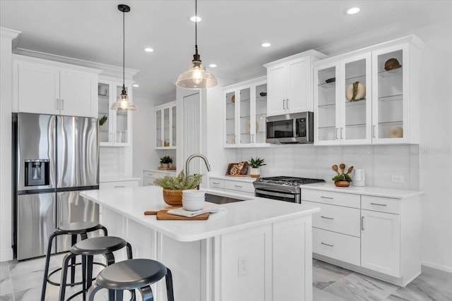 kitchen with backsplash, hanging light fixtures, an island with sink, appliances with stainless steel finishes, and white cabinetry