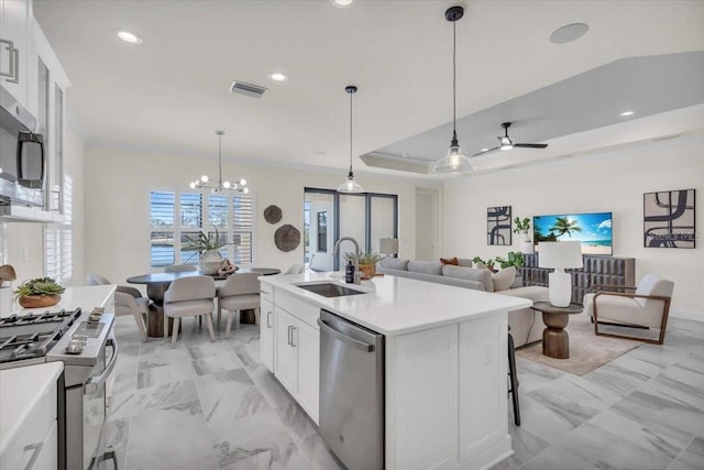 kitchen featuring white cabinetry, hanging light fixtures, a raised ceiling, a center island with sink, and appliances with stainless steel finishes