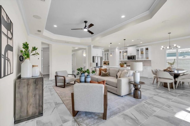 living room featuring a tray ceiling, ceiling fan with notable chandelier, and ornamental molding