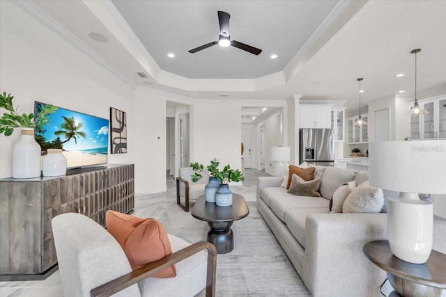 living room featuring a tray ceiling, ceiling fan, and ornamental molding