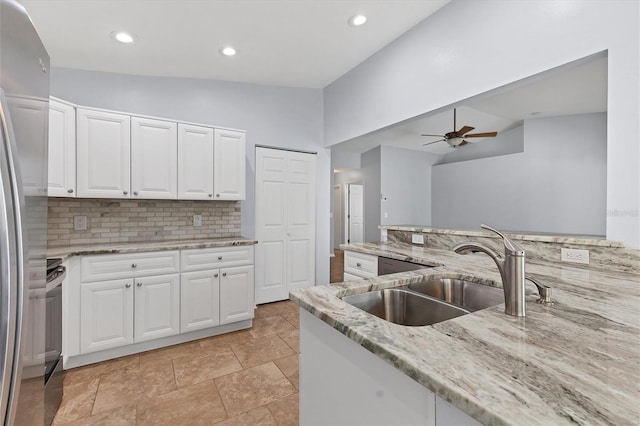 kitchen featuring vaulted ceiling, sink, stainless steel refrigerator, white cabinetry, and light stone countertops