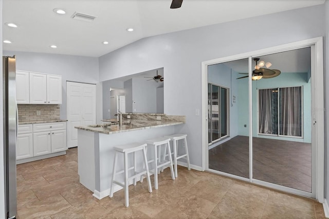 kitchen featuring lofted ceiling, white cabinetry, sink, kitchen peninsula, and stainless steel refrigerator