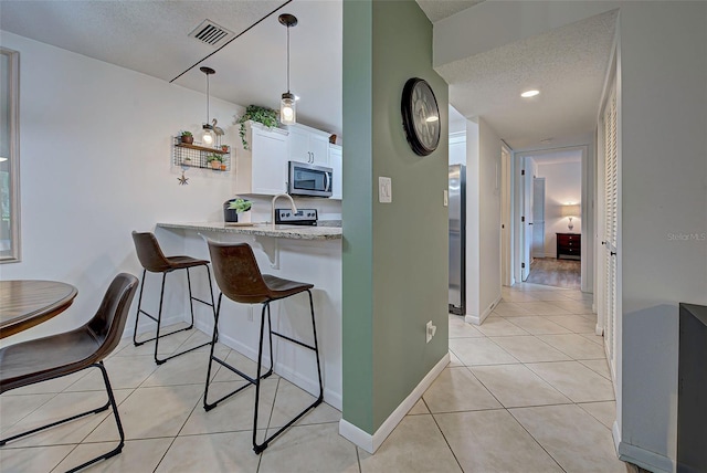 kitchen with light stone countertops, light tile patterned floors, pendant lighting, white cabinets, and appliances with stainless steel finishes