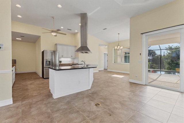 kitchen featuring stainless steel fridge with ice dispenser, a sink, dark countertops, ceiling fan with notable chandelier, and island range hood