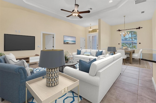 living area with a raised ceiling, light tile patterned flooring, visible vents, and ceiling fan