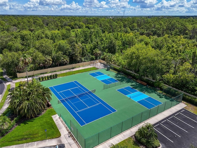 view of tennis court with a wooded view and fence