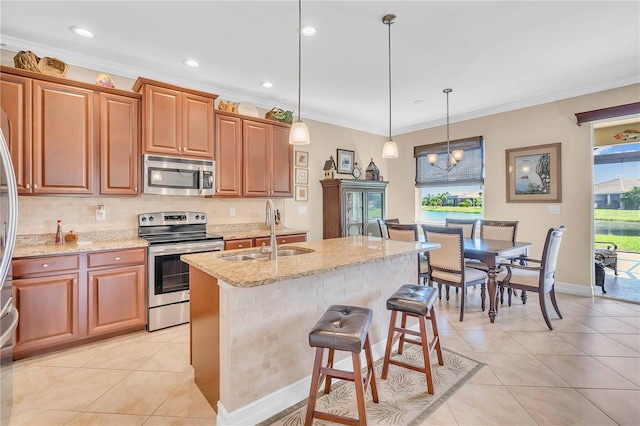 kitchen featuring sink, light stone counters, decorative light fixtures, appliances with stainless steel finishes, and a kitchen island with sink