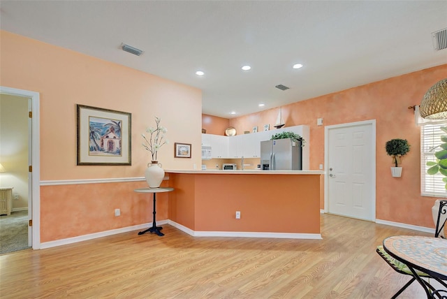 kitchen featuring white cabinetry, kitchen peninsula, light hardwood / wood-style floors, and stainless steel fridge with ice dispenser