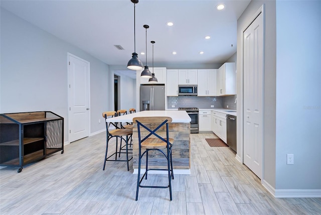 kitchen with white cabinetry, a center island, stainless steel appliances, light hardwood / wood-style flooring, and pendant lighting