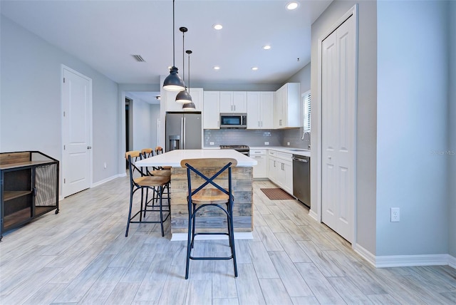 kitchen with white cabinets, hanging light fixtures, sink, appliances with stainless steel finishes, and a kitchen island