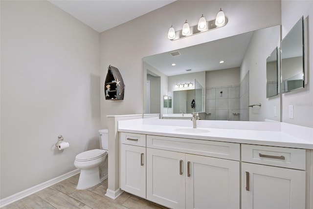 bathroom with a tile shower, vanity, and toilet