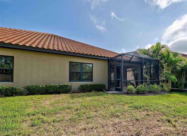 rear view of property featuring glass enclosure and a yard