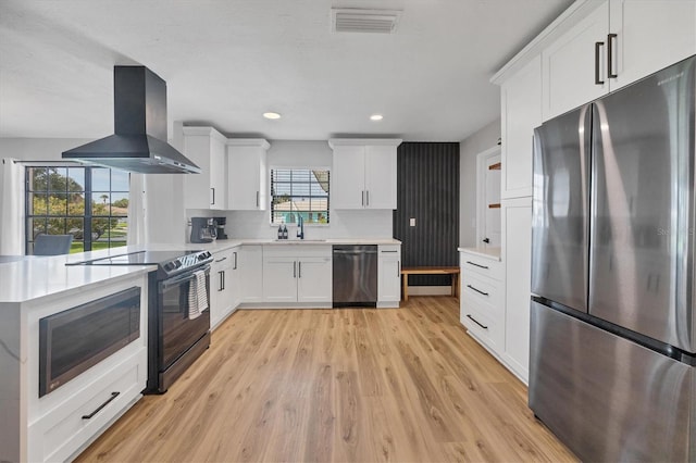 kitchen with appliances with stainless steel finishes, light wood-type flooring, sink, white cabinetry, and range hood