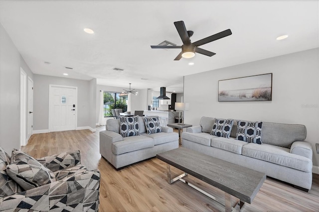 living room featuring ceiling fan with notable chandelier and light hardwood / wood-style flooring