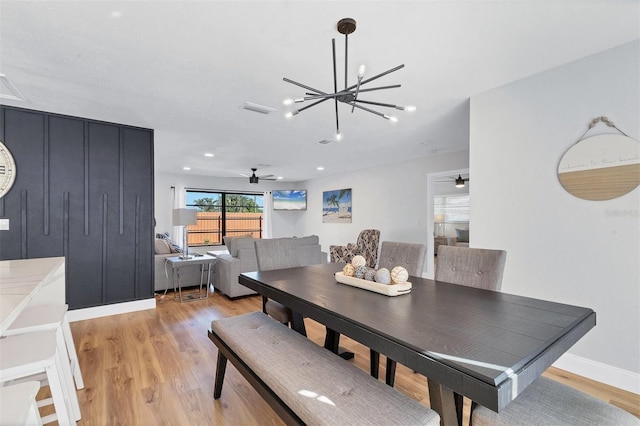 dining area with ceiling fan with notable chandelier and light hardwood / wood-style flooring