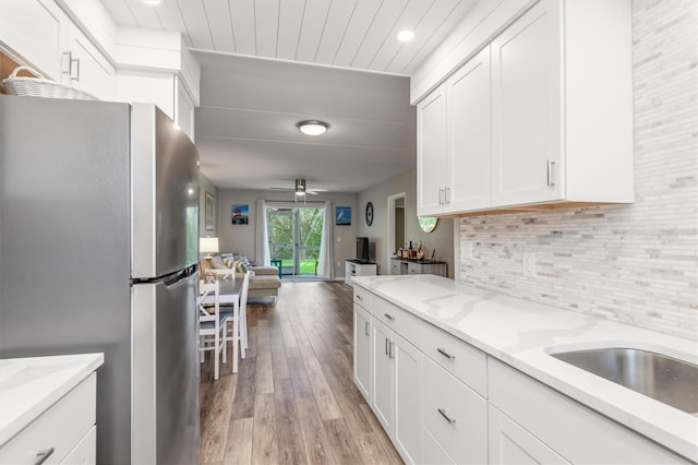 kitchen featuring ceiling fan, light hardwood / wood-style floors, white cabinets, stainless steel fridge, and light stone counters