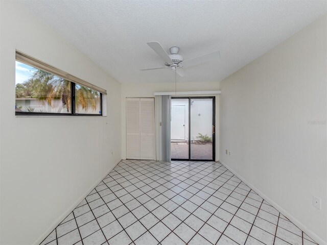 empty room featuring a textured ceiling, ceiling fan, a healthy amount of sunlight, and light tile patterned floors