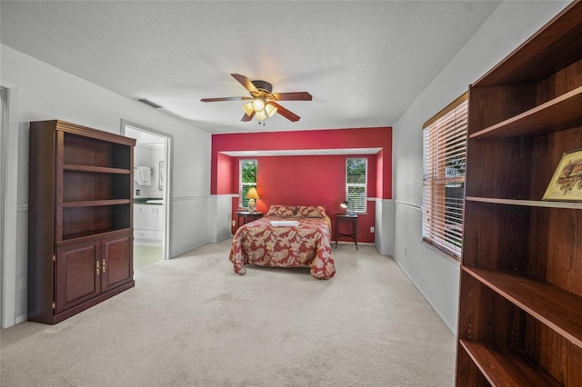 bedroom with ceiling fan, light colored carpet, and ensuite bath