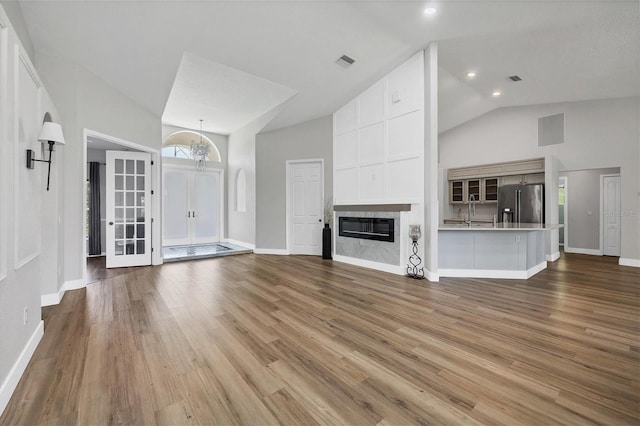 unfurnished living room with a large fireplace, high vaulted ceiling, light hardwood / wood-style floors, and sink