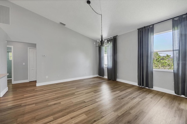 spare room featuring a chandelier, a healthy amount of sunlight, hardwood / wood-style floors, and a textured ceiling