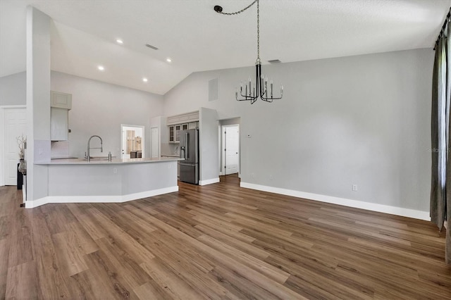 kitchen with high end refrigerator, a chandelier, high vaulted ceiling, kitchen peninsula, and dark hardwood / wood-style flooring