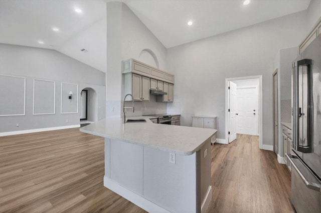 kitchen featuring appliances with stainless steel finishes, sink, kitchen peninsula, high vaulted ceiling, and light hardwood / wood-style flooring