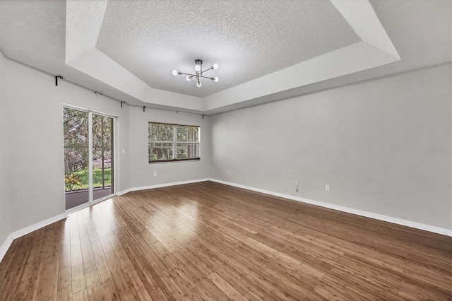 spare room with a chandelier, hardwood / wood-style floors, a textured ceiling, and a tray ceiling