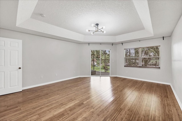 empty room with hardwood / wood-style flooring, a textured ceiling, a tray ceiling, and a chandelier