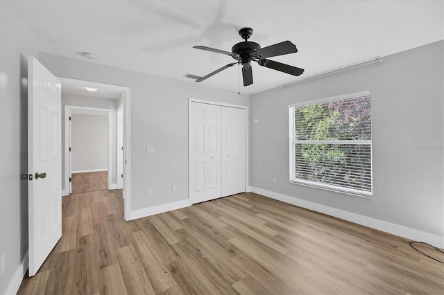 unfurnished bedroom with ceiling fan, a textured ceiling, a closet, and light wood-type flooring