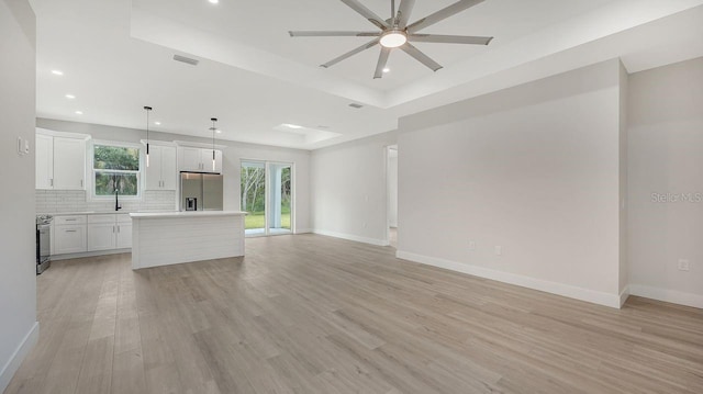 unfurnished living room with ceiling fan, sink, a raised ceiling, and light hardwood / wood-style floors