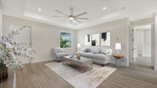 living room with a tray ceiling, ceiling fan, and hardwood / wood-style flooring