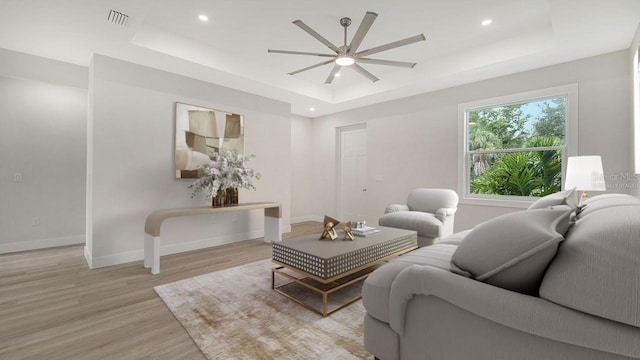 living room featuring ceiling fan, a tray ceiling, and light hardwood / wood-style flooring